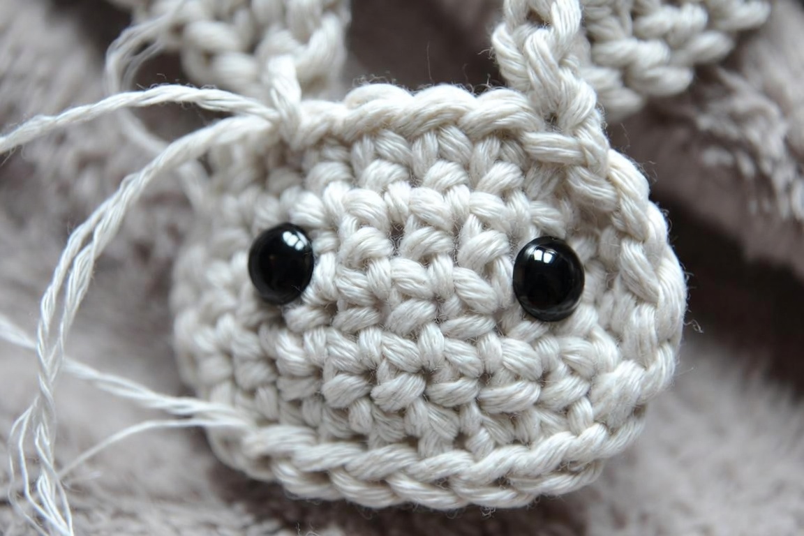 Close-up macro photo of a crochet bunny head in progress with black safety eyes installed